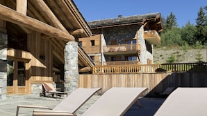 A wooden chalet with stone walls, a balcony, and lounge chairs. - CGH Résidences & Spas Les Cimes Blanches (Montvalezan)