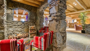 A rustic interior with stone walls, wooden beams, and a cozy seating area with striped chairs. - CGH Résidences & Spas Les Cimes Blanches (Montvalezan)