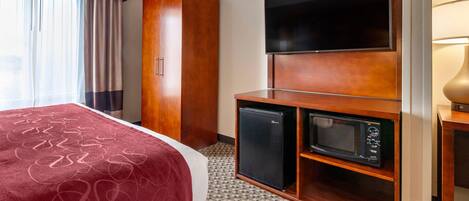 A hotel room with a bed, a minibar, a television, and a wardrobe.