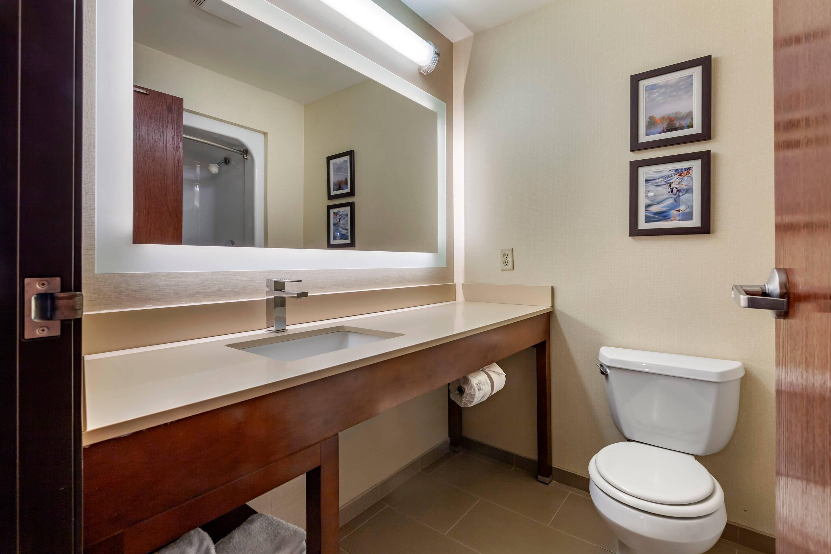 A bathroom with a sink, mirror, toilet, and framed pictures on the wall.