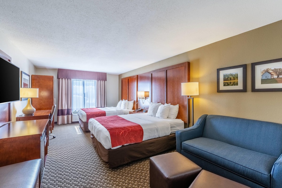 Ein Hotelzimmer mit zwei Betten, einem Schlafsofa, einem Schreibtisch und einem Fernseher.