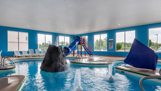 Una piscina interior con tobogán de agua, sillas de descanso y vistas al exterior.