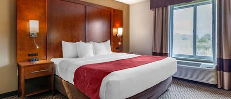 A hotel room with a large bed, a nightstand, a wall-mounted lamp, and a window with curtains.
