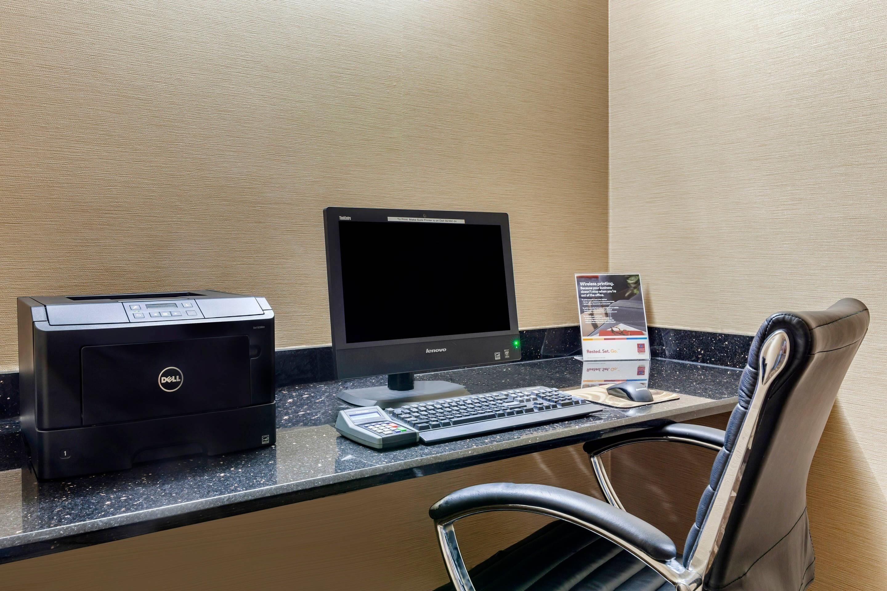 A hotel reception desk with a desktop computer, a printer, a keyboard, a mouse, and a chair.