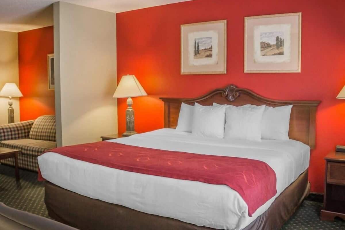 Ein Hotelzimmer mit einem großen Bett, zwei Nachttischen, einem Sessel und zwei gerahmten Bildern an der Wand.
