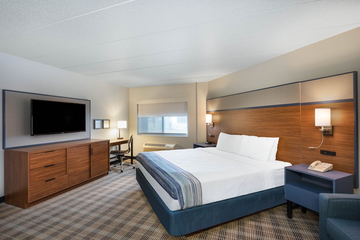 Habitación de hotel con una cama grande, un escritorio, un televisor de pantalla plana, cabecera de madera y mesita de noche con teléfono.