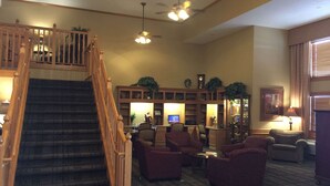 A spacious lobby with a staircase, multiple seating areas, and a large wooden bookshelf. - AmericInn by Wyndham Jackson (Jackson)