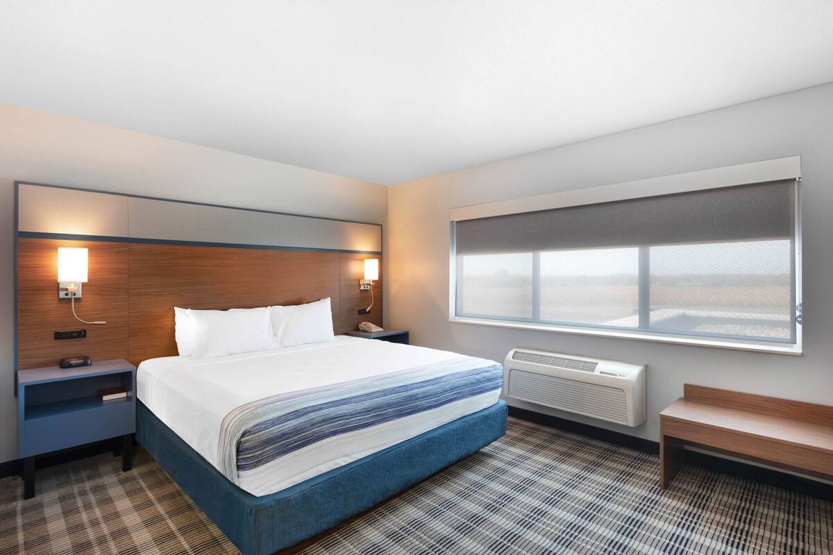 Una habitación de hotel con cama, mesitas de noche, calefacción, una ventana con vistas y un banco.
