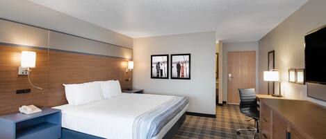 Une chambre d’hôtel comprenant un lit, des tables de chevet, un bureau, une chaise et un téléviseur.
