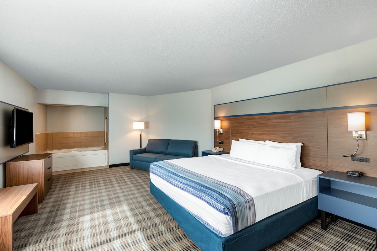 Una habitación de hotel con cama, escritorio, silla, televisor y baño.