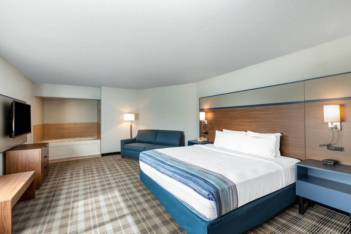 Una habitación de hotel con cama, escritorio, silla, televisor y baño.