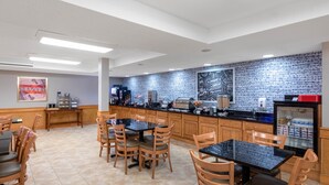 A modern kitchen with a brick backsplash, wooden cabinets, and a central island. There are multiple seating areas with tables and chairs. - AmericInn by Wyndham Jackson (Jackson)