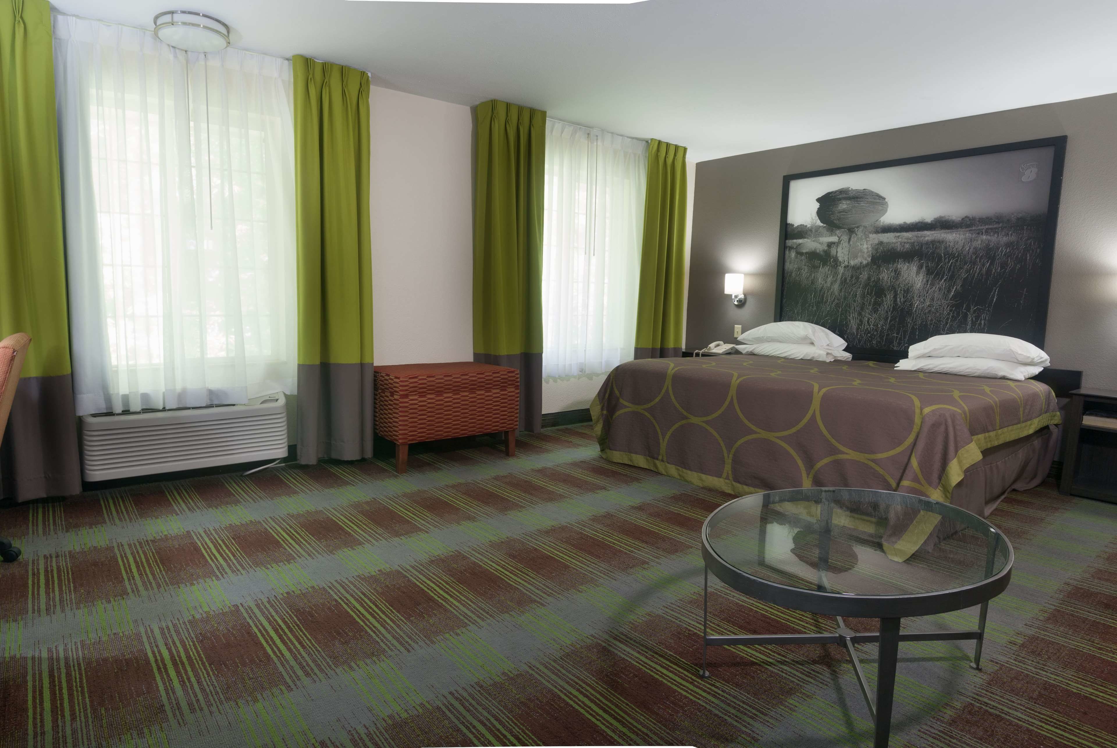 A hotel room with a bed, a round glass table, a bench, and a large painting on the wall.