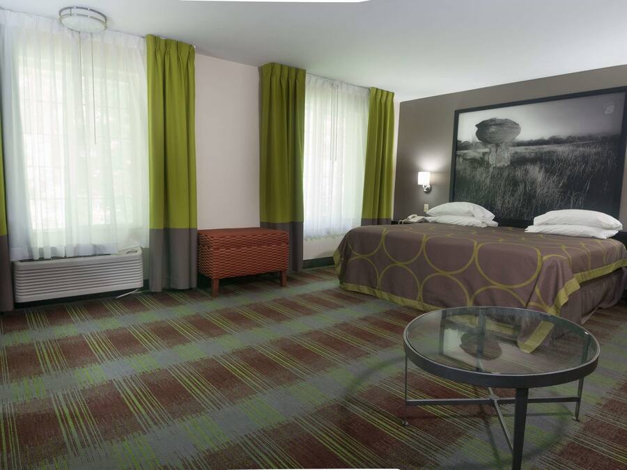 A hotel room with a bed, a round glass table, a bench, and a large painting on the wall.