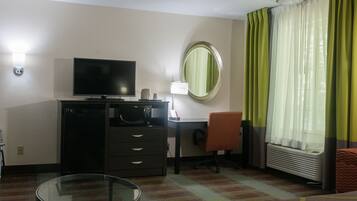Une chambre d’hôtel équipée d’un téléviseur à écran plat, d’un bureau, d’une chaise, d’une petite table, d’un miroir et d’une fenêtre avec des rideaux.
