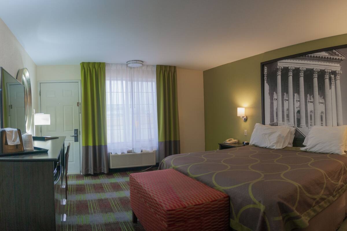 A hotel room with a large bed, a desk with a lamp, a telephone, and a framed picture on the wall.