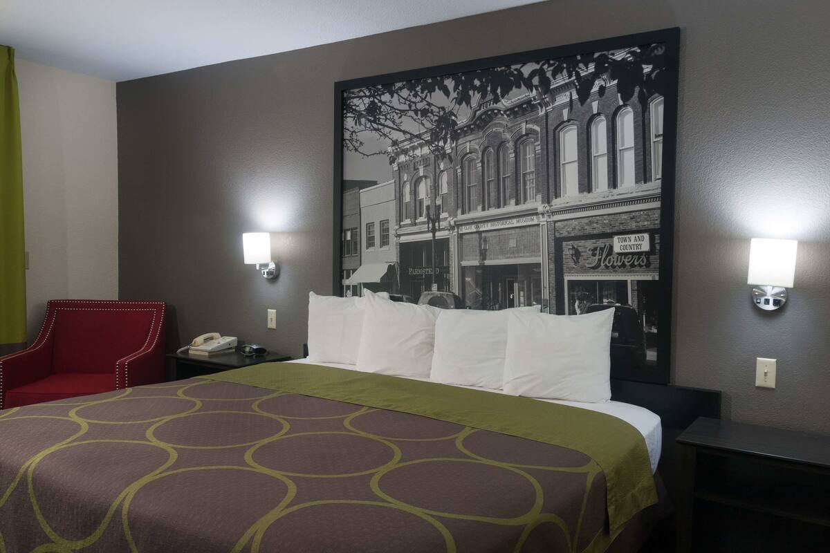 A hotel room with a bed, a red armchair, two bedside tables with lamps, and a large framed picture on the wall.