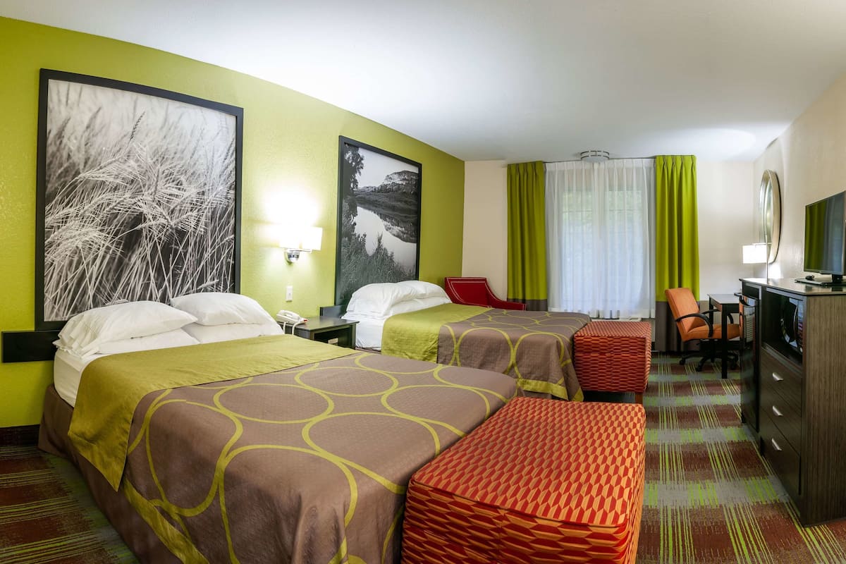 A hotel room with two beds, a desk, a chair, a TV, and artwork on the walls.