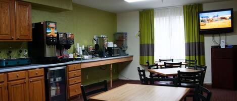 A compact hotel room with a kitchenette, a dining area, and a TV mounted on the wall.