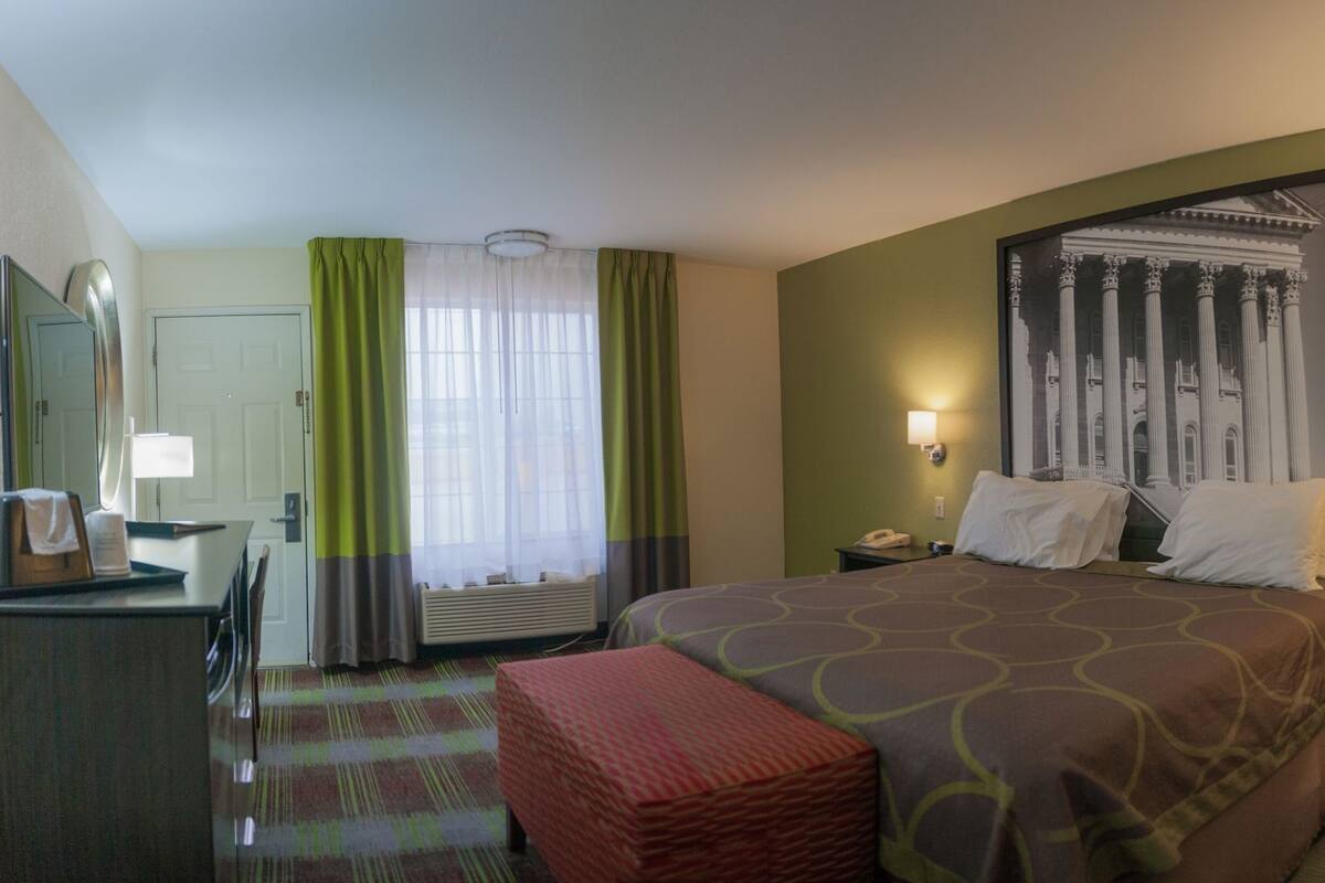 A hotel room with a bed, a desk, a chair, a telephone, and a window with curtains.