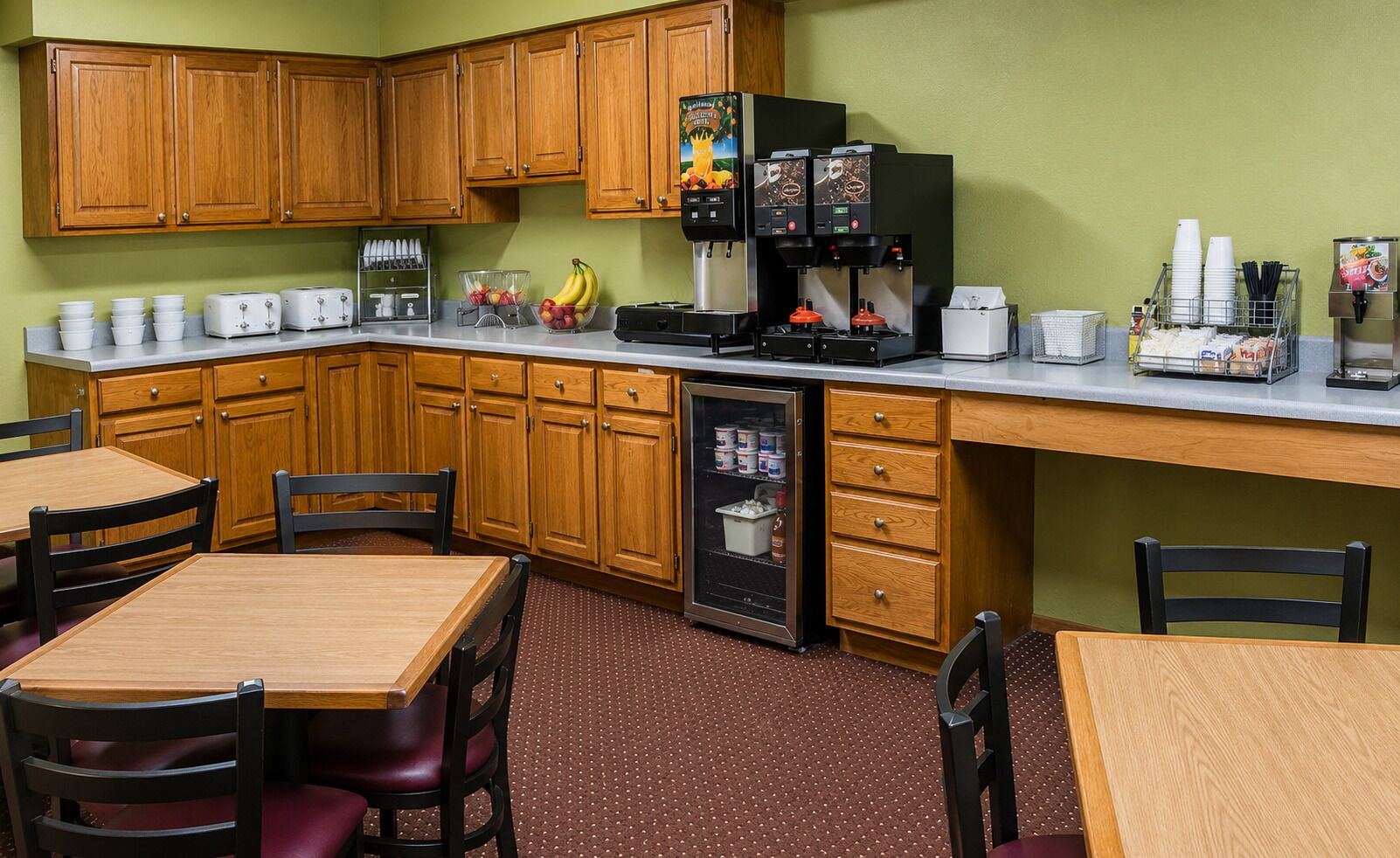 A compact kitchen with wooden cabinets, a refrigerator, a coffee machine, and a microwave. There are two wooden tables with chairs, and a small refrigerator with a freezer drawer.