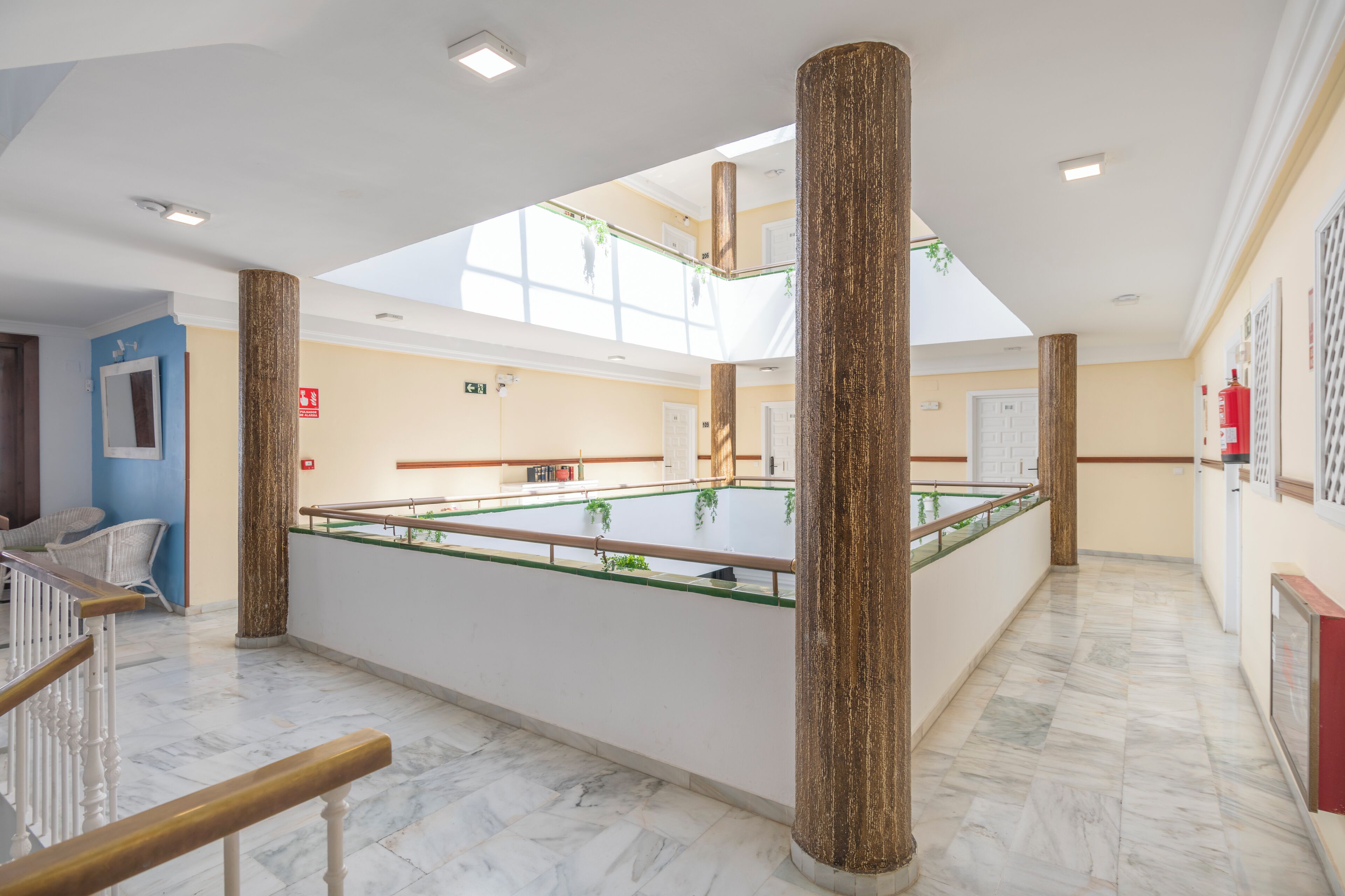 Un vaste espace intérieur doté d’une table en verre au centre, de piliers en bois et d’un haut plafond agrémenté de lucarnes.