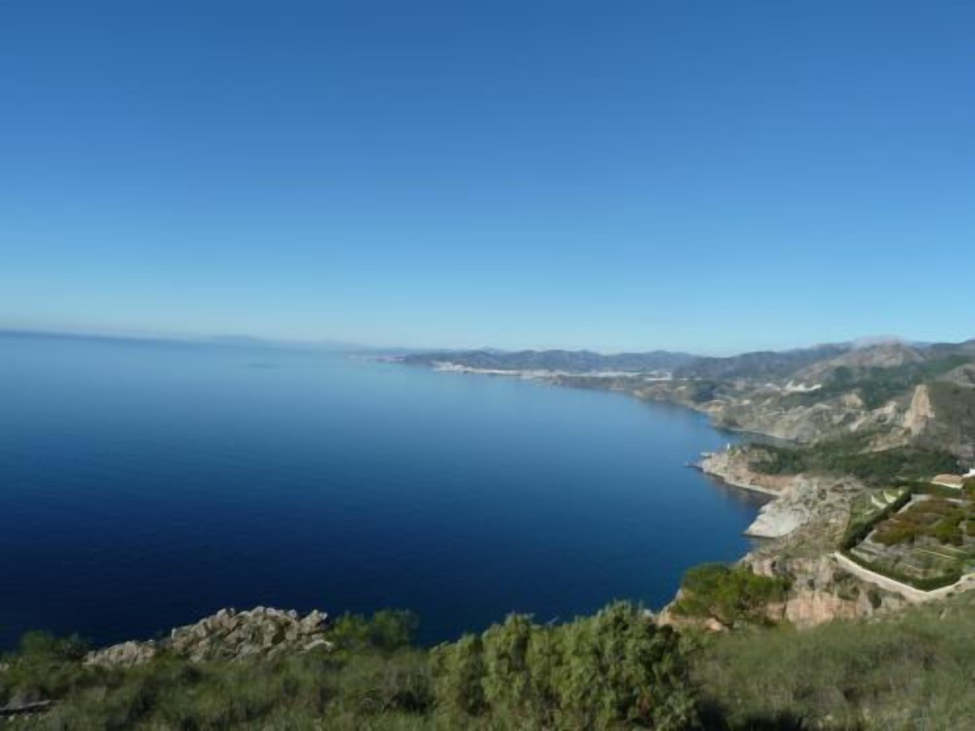 Un paisaje costero con vistas despejadas al mar y montañas a lo lejos.