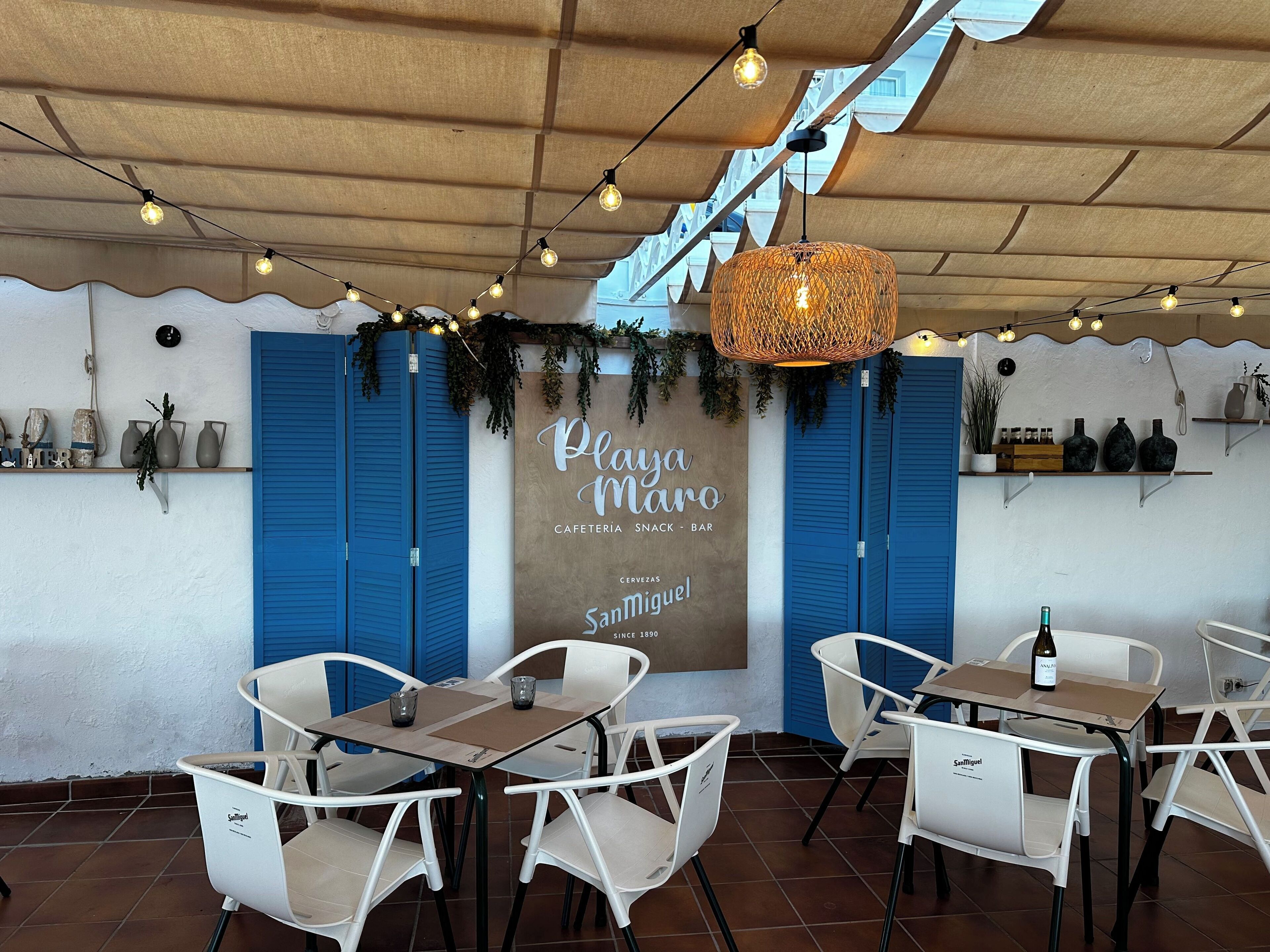 A café with blue shutters, white chairs, and a hanging wicker light fixture.