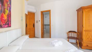 Habitación de hotel con cama, armario de madera, una silla y baño visible a través de una puerta abierta.