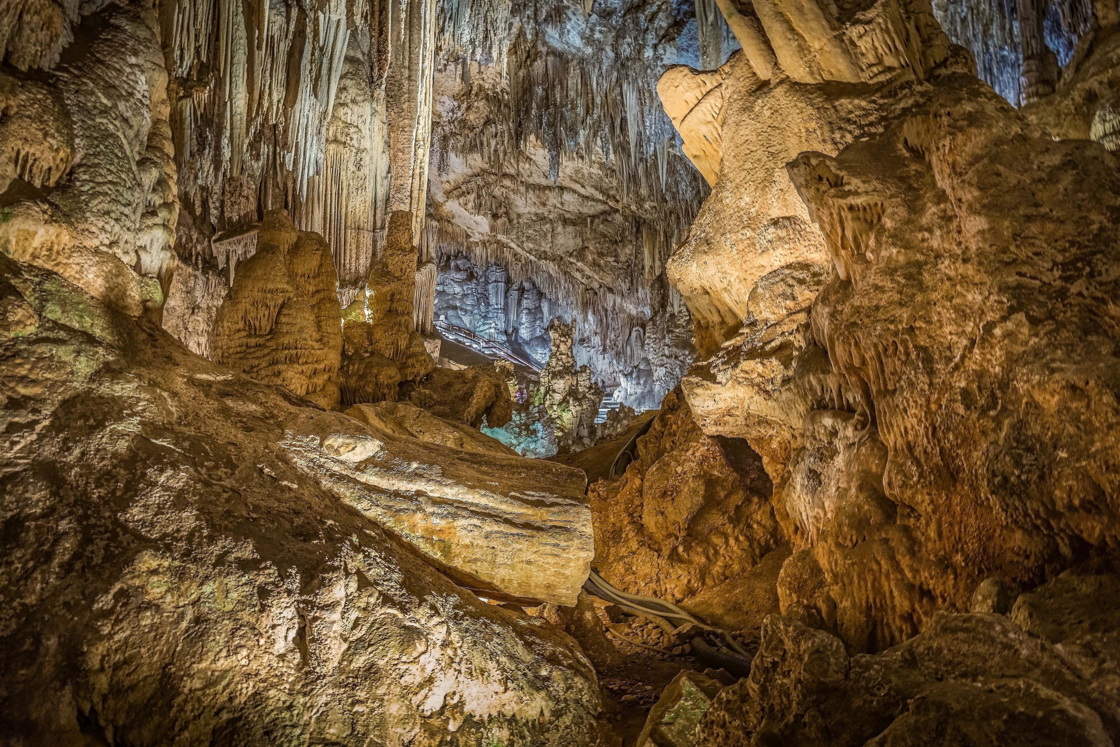 Interior de caverna com estalactites e estalagmites, iluminado por luz artificial.