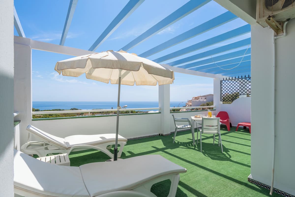 Ein Balkon mit einem weißen Tisch, Stühlen und einem beige farbenen Sonnenschirm.