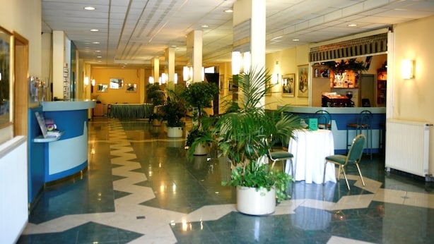 Un hall d’hôtel comprenant un comptoir d’accueil, des plantes en pot et un espace repas.