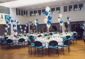 A banquet hall with tables set for a formal event, featuring blue and white balloon decorations.