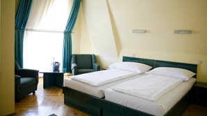 Une chambre d’hôtel avec deux lits simples, une chaise, une petite table et une fenêtre avec des rideaux.