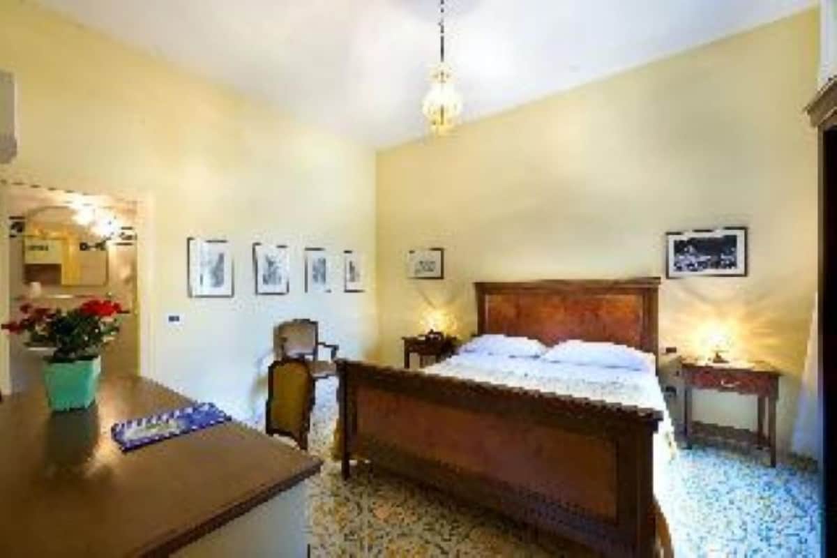 A bedroom with a wooden bed, a desk with a chair, and a small table with a lamp.