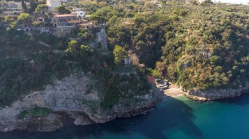 Vista aérea de una zona costera con un acantilado, un edificio pequeño y un mar azul cristalino.