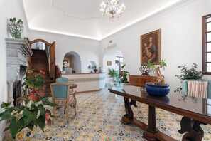 A spacious room with a patterned floor, a wooden staircase, a dining table with chairs, and a large painting on the wall.