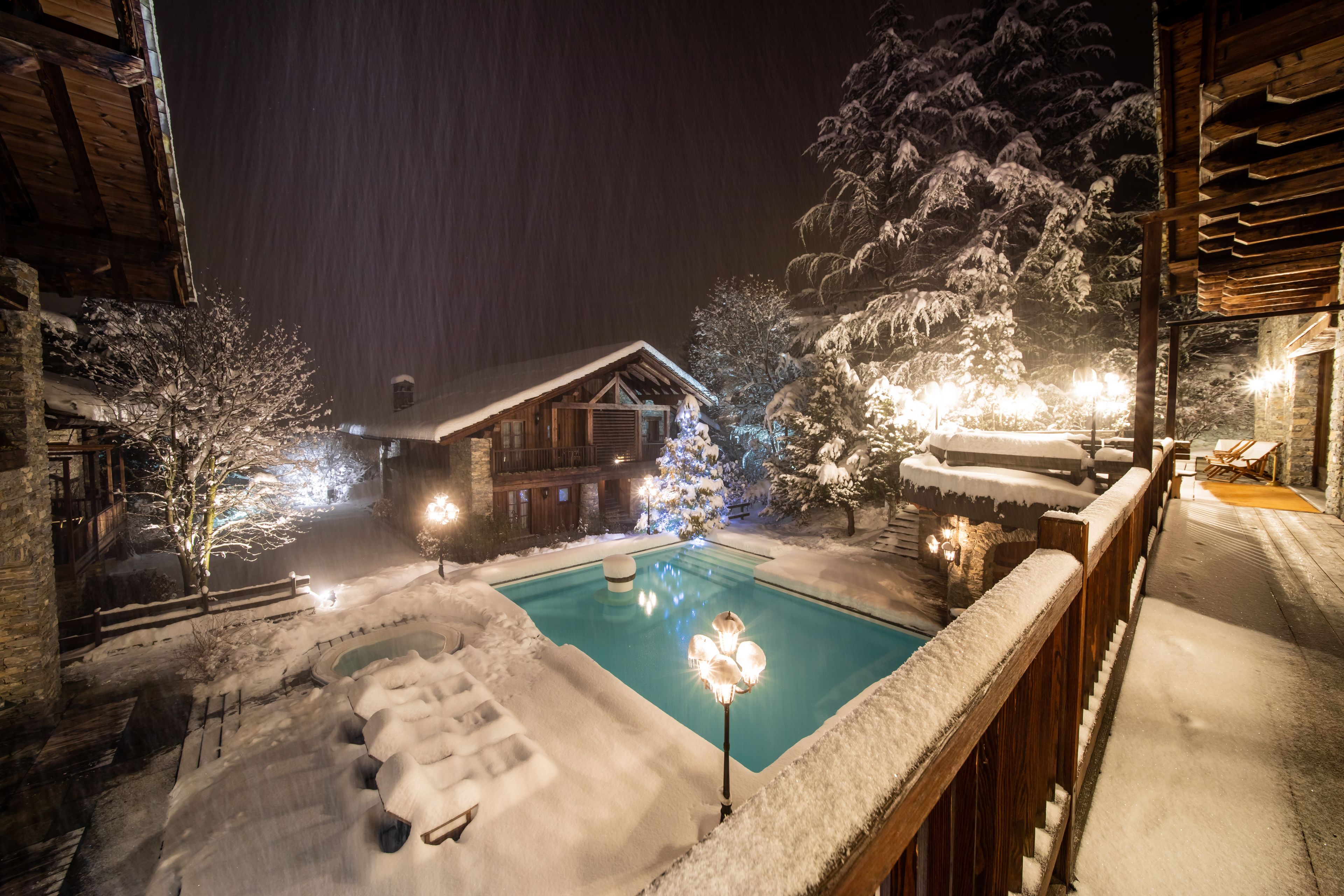 A snow-covered outdoor pool area with a wooden deck and a wooden cabin in the background.