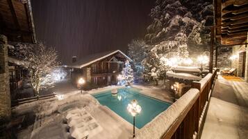 A snow-covered outdoor pool area with a wooden deck and a wooden cabin in the background.