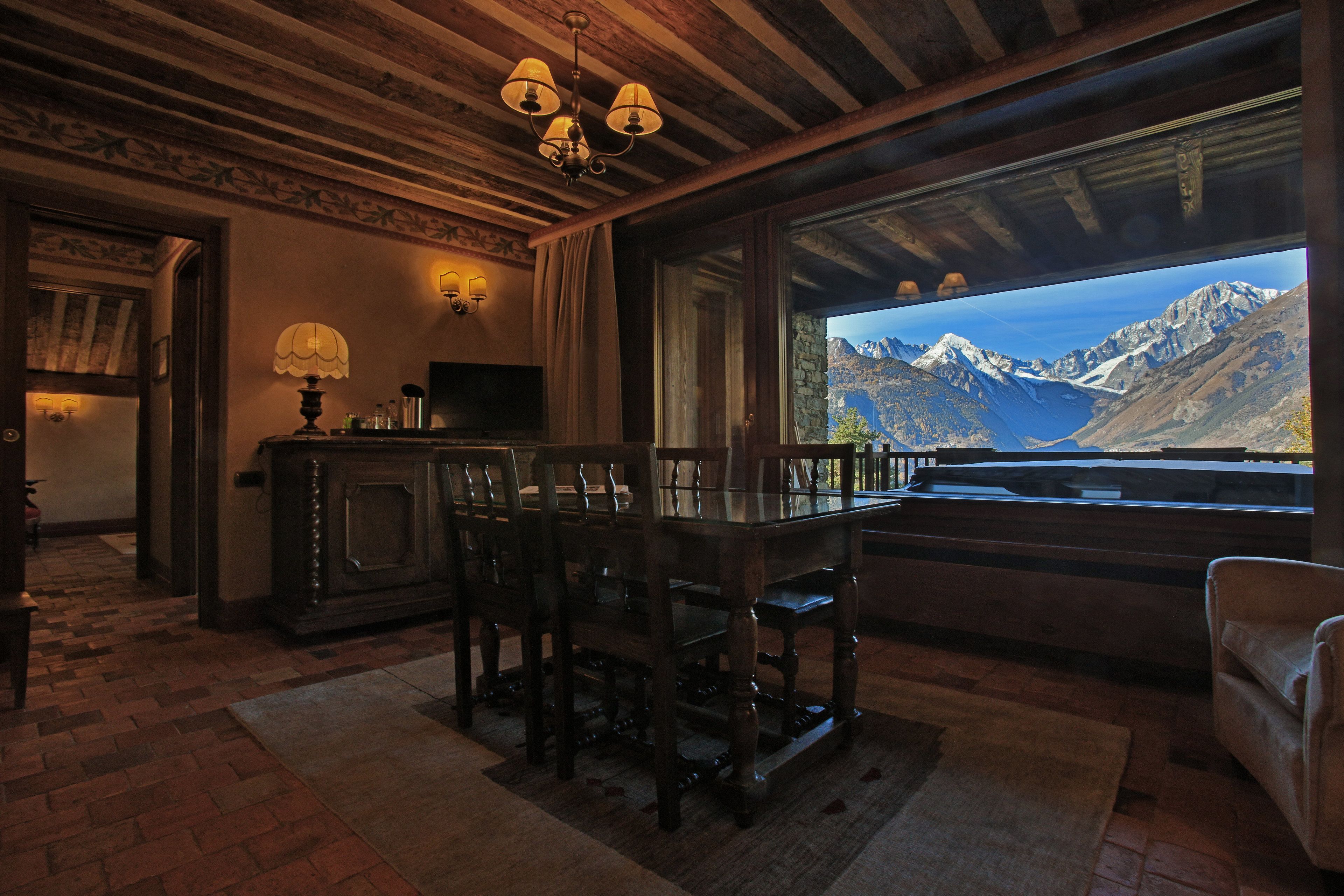 Una stanza accogliente con soffitto in legno, un tavolo da pranzo con sedie, una televisione e un'ampia finestra con vista sulle montagne.