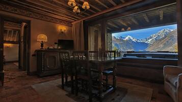 Una stanza accogliente con soffitto in legno, un tavolo da pranzo con sedie, una televisione e un'ampia finestra con vista sulle montagne.