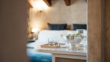 A bed with pillows, a bedside table with a bowl of apples and glasses, and a lamp.
