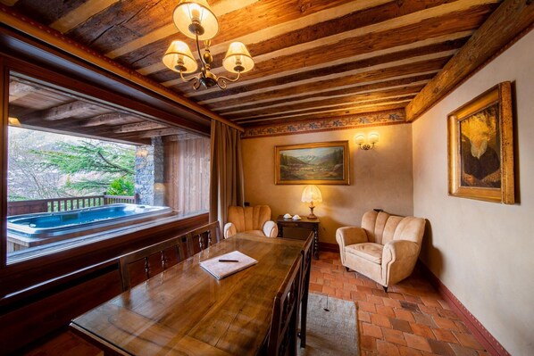 A wooden dining room with a large table, chairs, a fireplace, and a view of a hot tub outside.