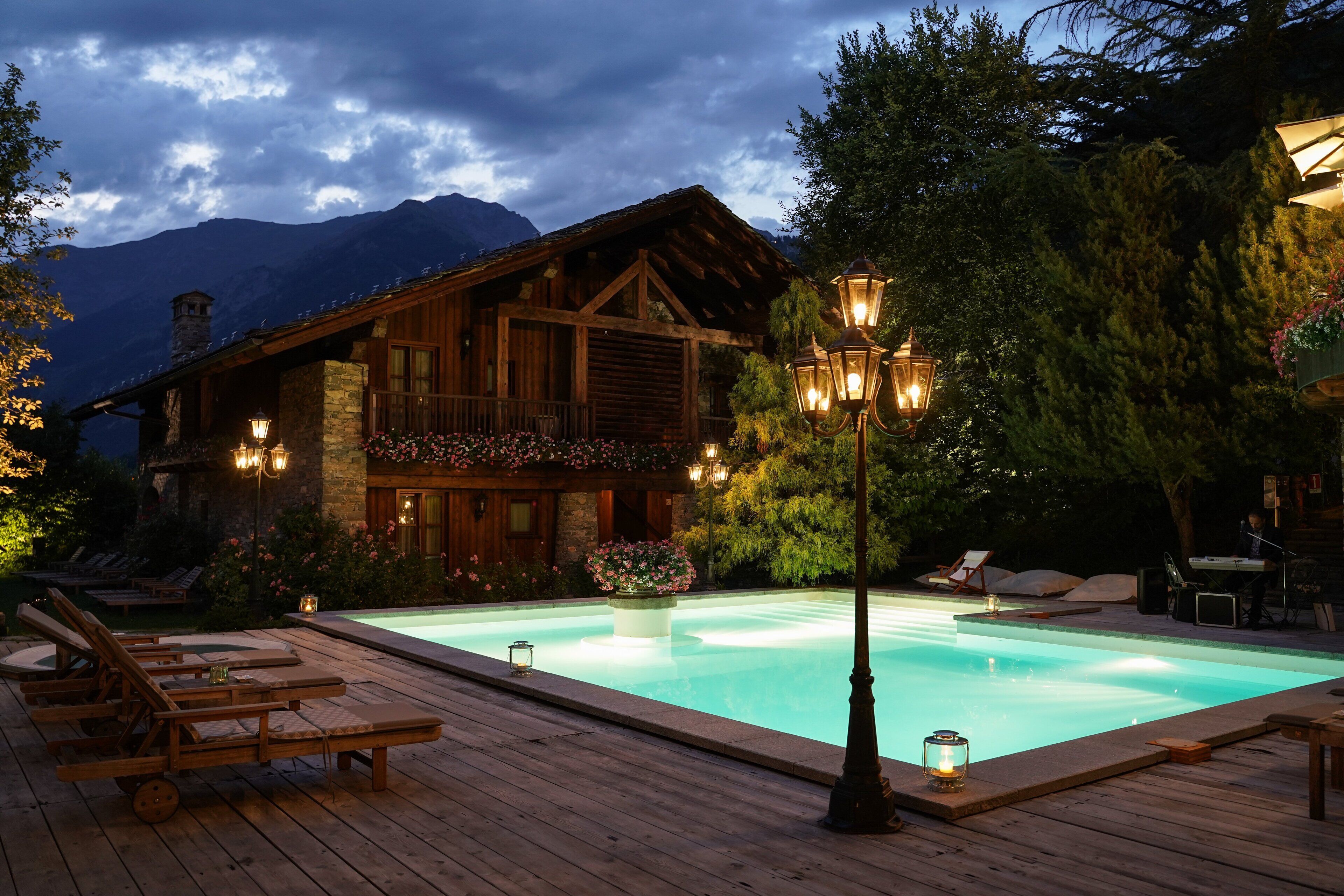 A wooden cabin with a swimming pool, surrounded by trees and mountains.