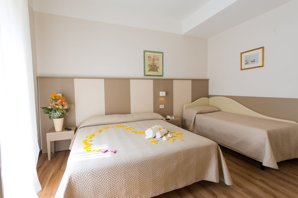 A hotel room with two beds, a bedside table with a vase of flowers, and a wall-mounted picture.