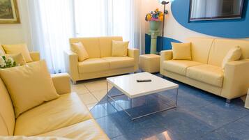 Una sala de estar con tres sofás color crema, una mesa de centro blanca y un piso de baldosas azules.
