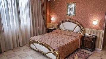 Ein Schlafzimmer mit Bett, Vorhängen, einer Chandelierleuchtre, einem Nachttisch und einer Wandlampe.