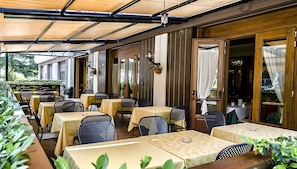 An outdoor cafe with tables and chairs, covered by a canopy, and wooden walls.