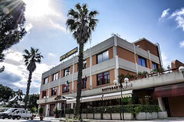 A hotel with a sign reading "HOTEL SORRISO" and a restaurant named "HOTEL SORRISO RISTORANTE" below it.