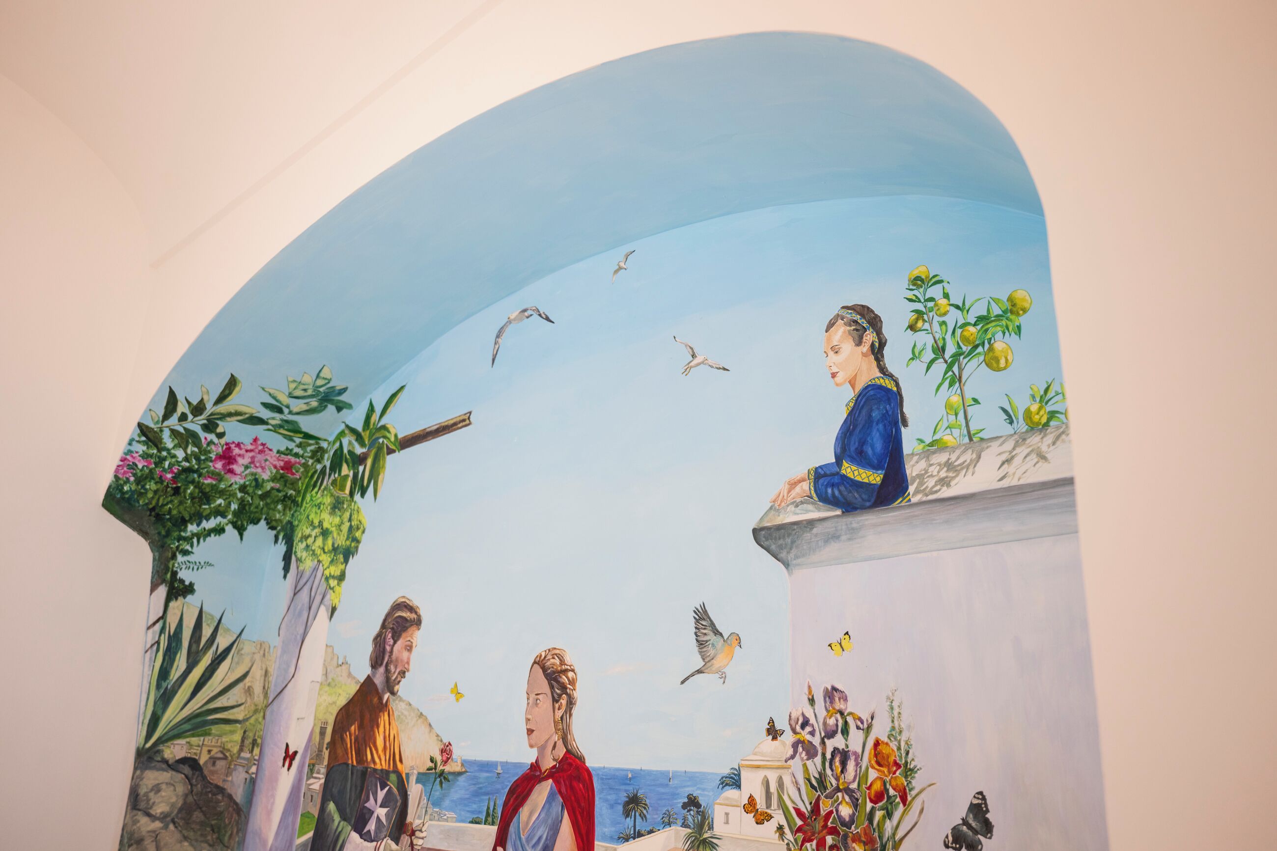 A mural with a coastal scene, including a person on a balcony, a body of water, and birds in the sky.